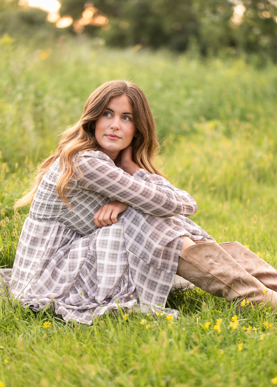 Taupe plaid maxi dress swaying in a field, showing the tiered skirt's movement at sunset.