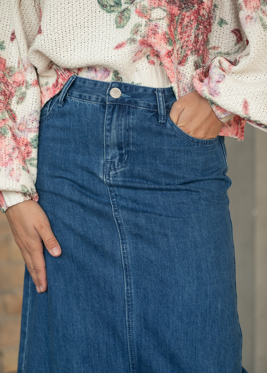 Close-up of medium-wash denim skirt waistband with button closure, belt loops, and front pocket.