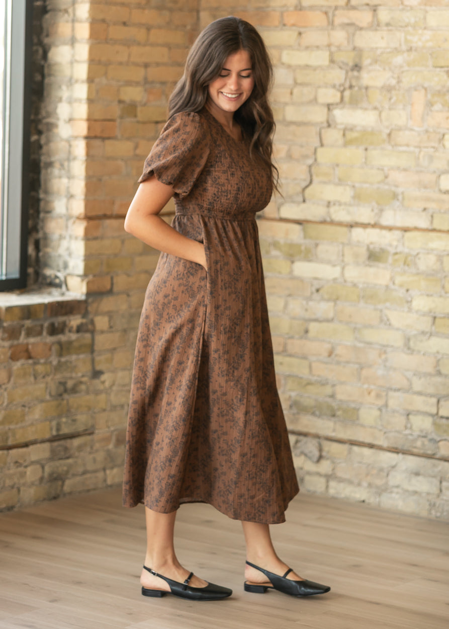 Full-length brown floral midi dress with puff sleeves and flowing skirt, styled with black flats.