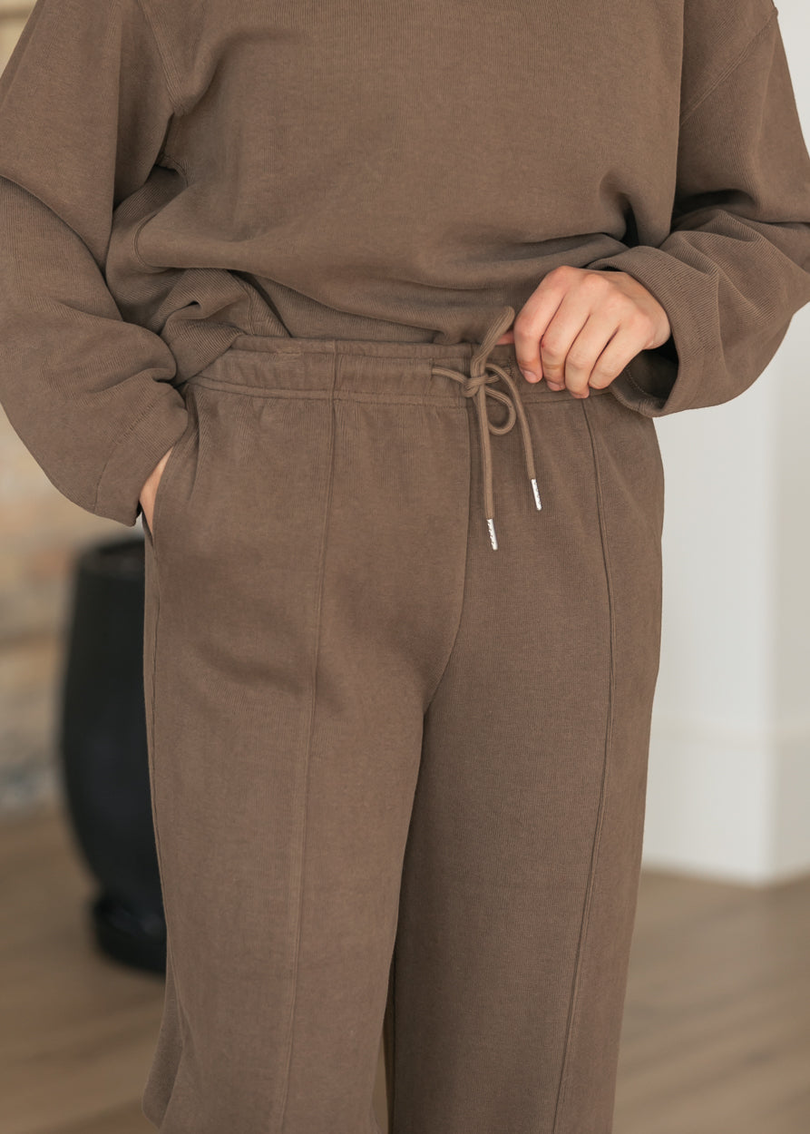 Close-up of brown wide leg joggers showing drawstring waistband, side pocket, and vertical pintuck seams.