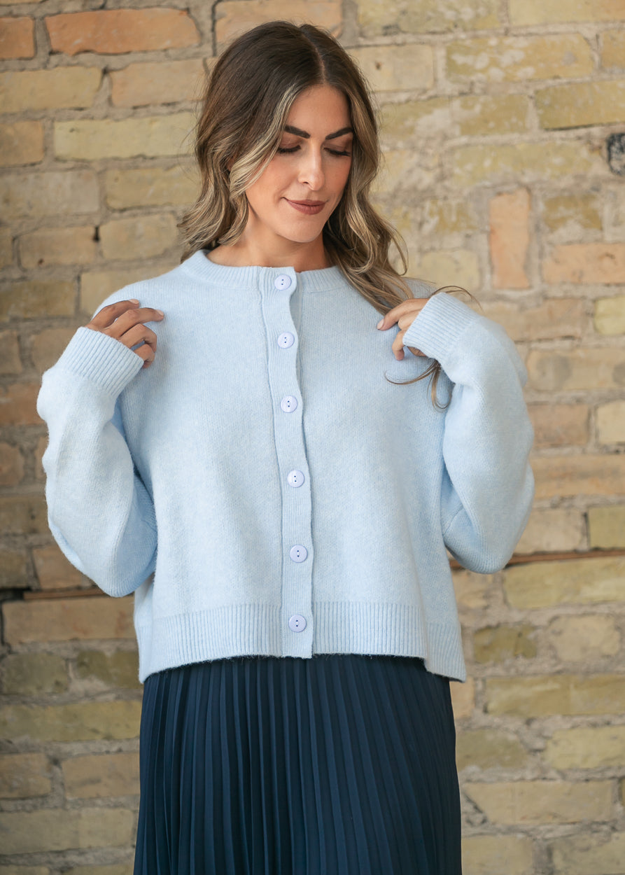 Powder blue button-down cardigan styled with a flowy navy pleated midi skirt.