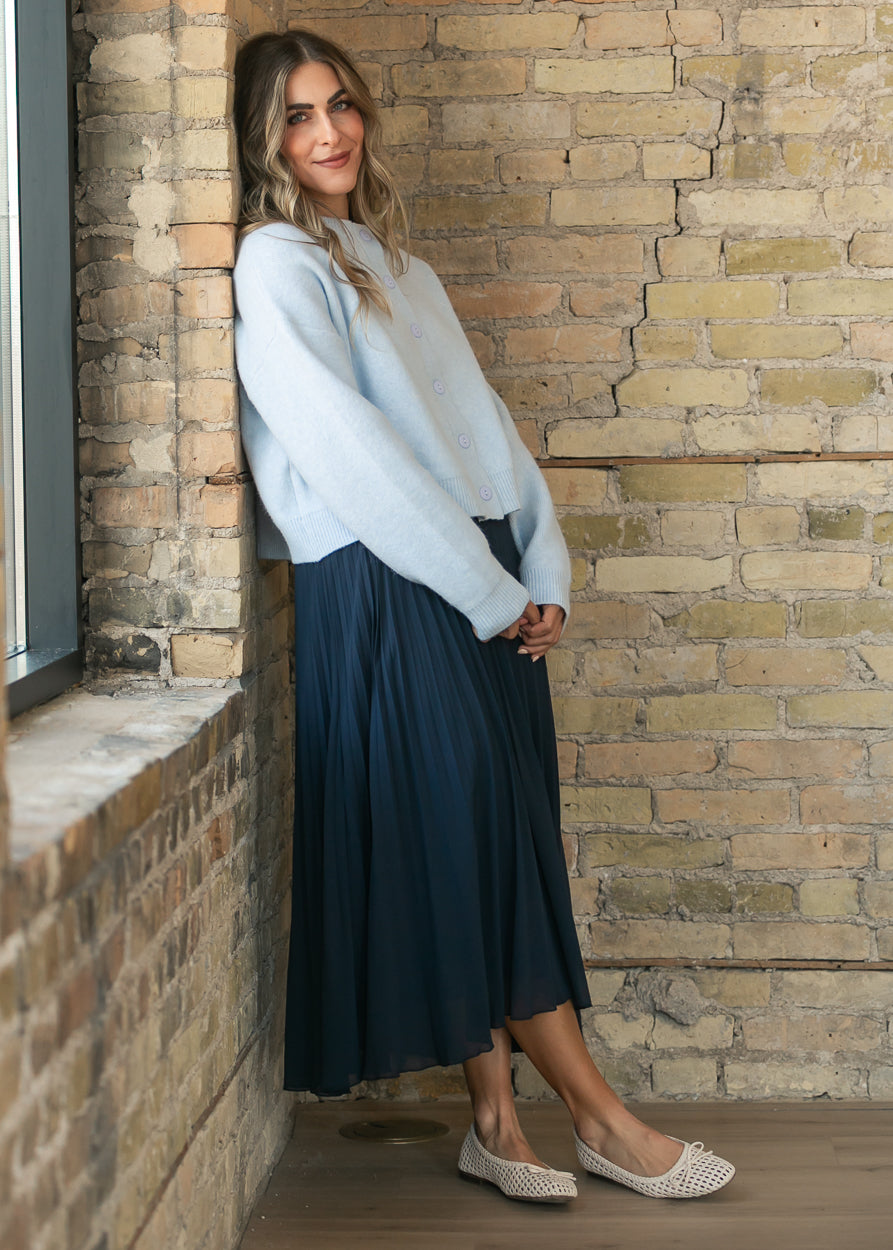 Navy flowy pleated midi skirt styled with a light blue cardigan and woven flats.