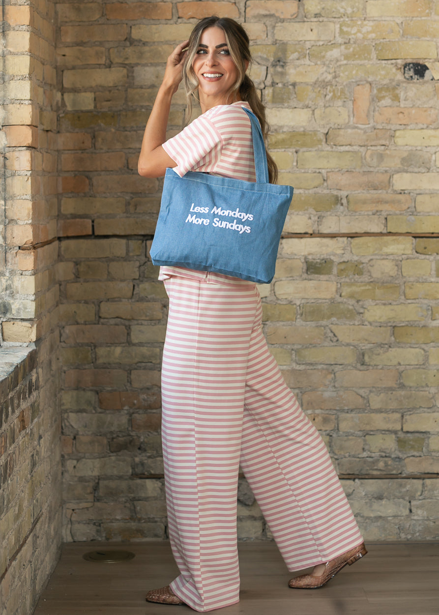 Medium wash denim tote carried over the shoulder with long straps and embroidered front lettering.