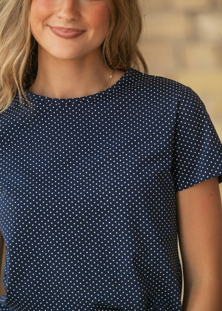 Close-up of navy polka dot jersey tee showing the crew neckline, short sleeves, and tiny white dot print.