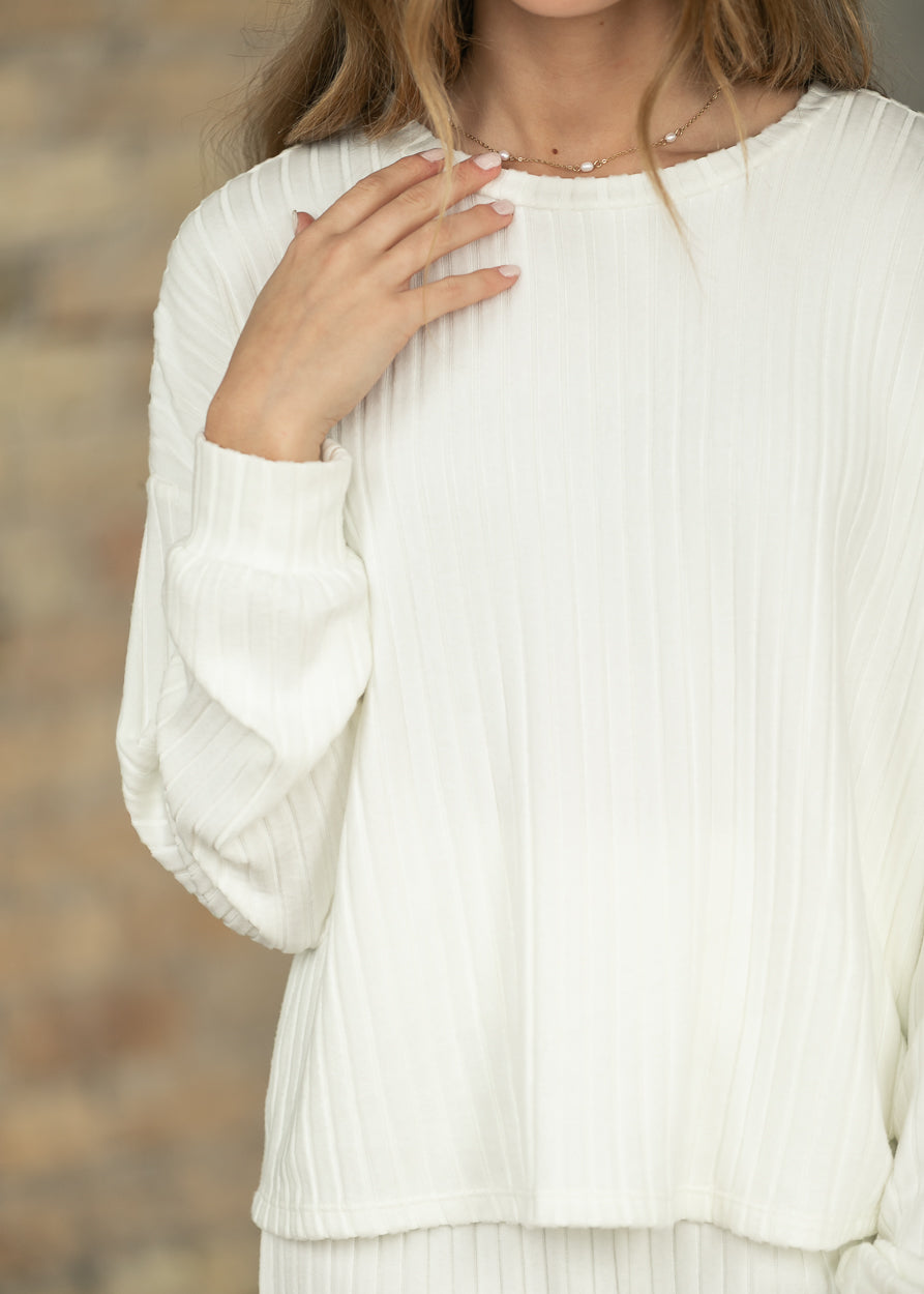 Close-up of bone white ribbed top showing vertical rib texture, crew neckline, and long sleeve cuff.