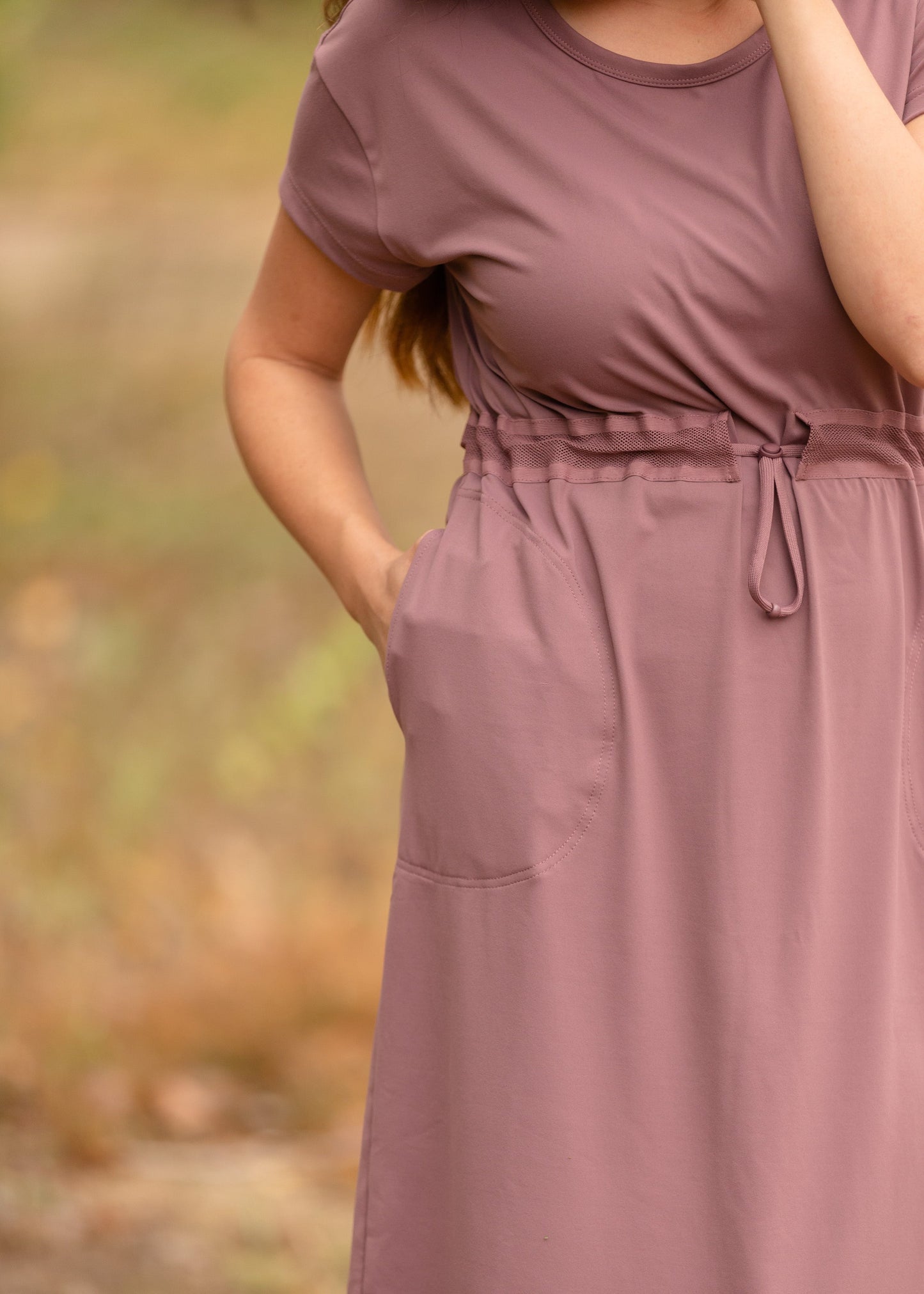 This is a Cinch Waist Athletic midi dress in a purpley taupe color that has a mesh detail and large side pockets.