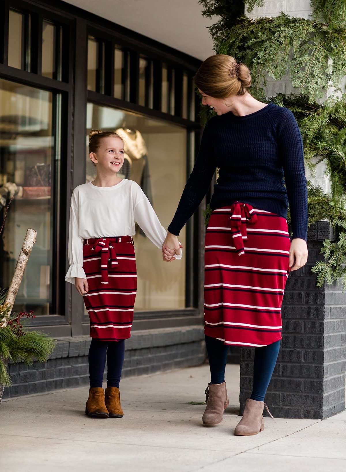 Woman wearing a modest mustard and burgandy striped midi skirt. This skirt has a fabric belt that is removable and is also mommy and me styled. This skirt is paired with tights and boots.
