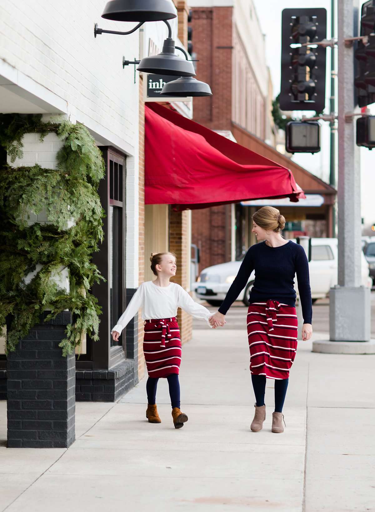 Woman wearing a modest mustard and burgandy striped midi skirt. This skirt has a fabric belt that is removable and is also mommy and me styled. This skirt is paired with tights and boots.