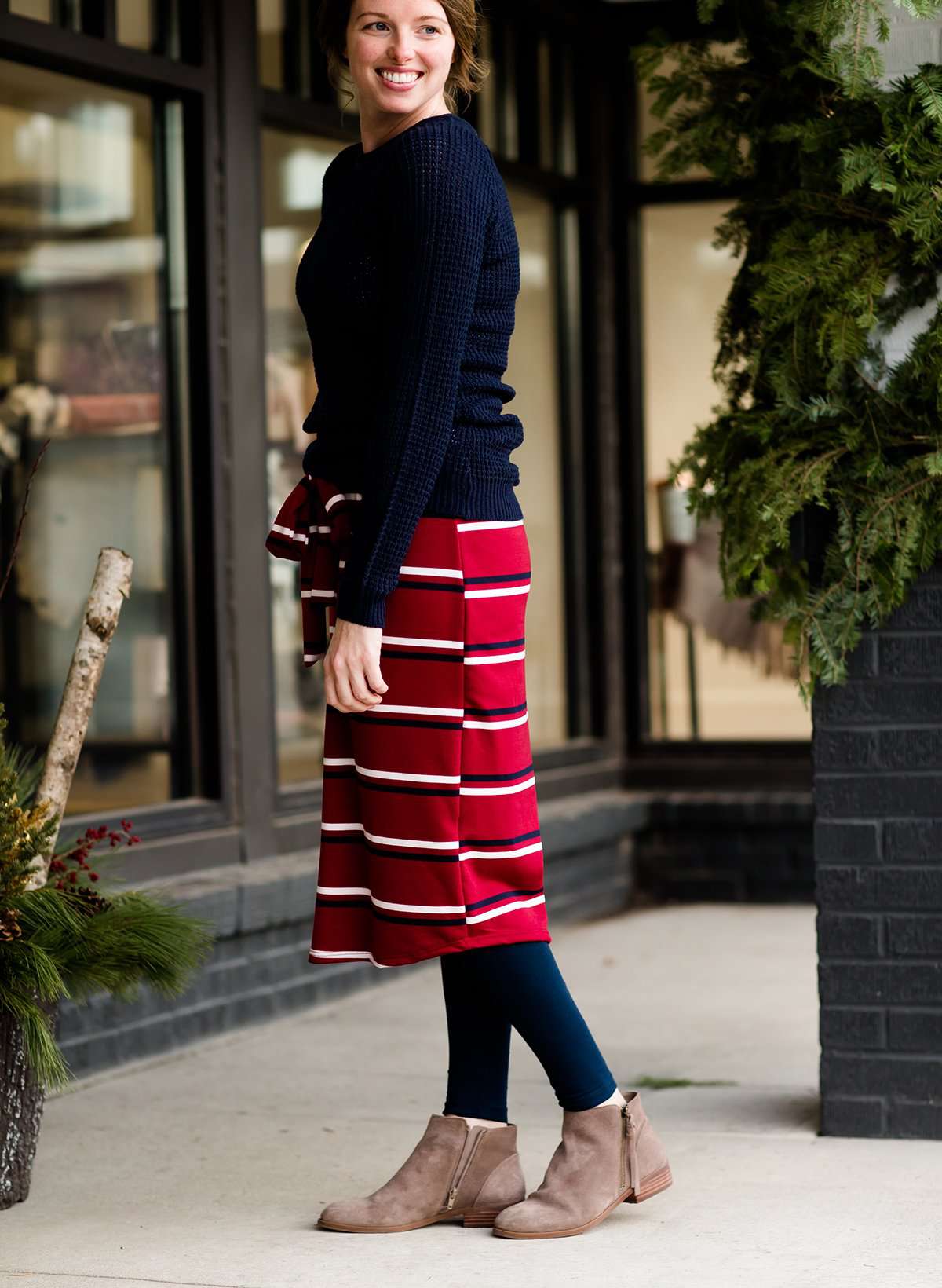 Woman wearing a modest mustard and burgandy striped midi skirt. This skirt has a fabric belt that is removable and is also mommy and me styled. This skirt is paired with tights and boots.