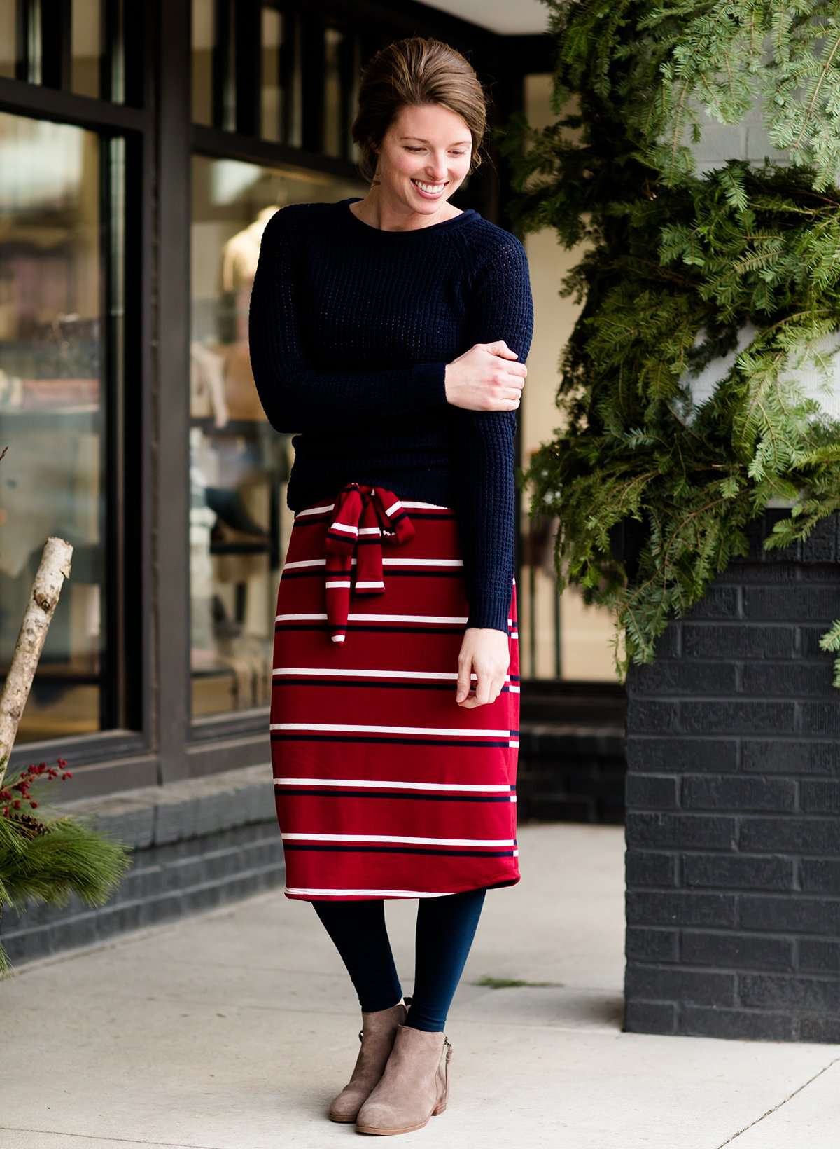 Woman wearing a modest mustard and burgandy striped midi skirt. This skirt has a fabric belt that is removable and is also mommy and me styled. This skirt is paired with tights and boots.