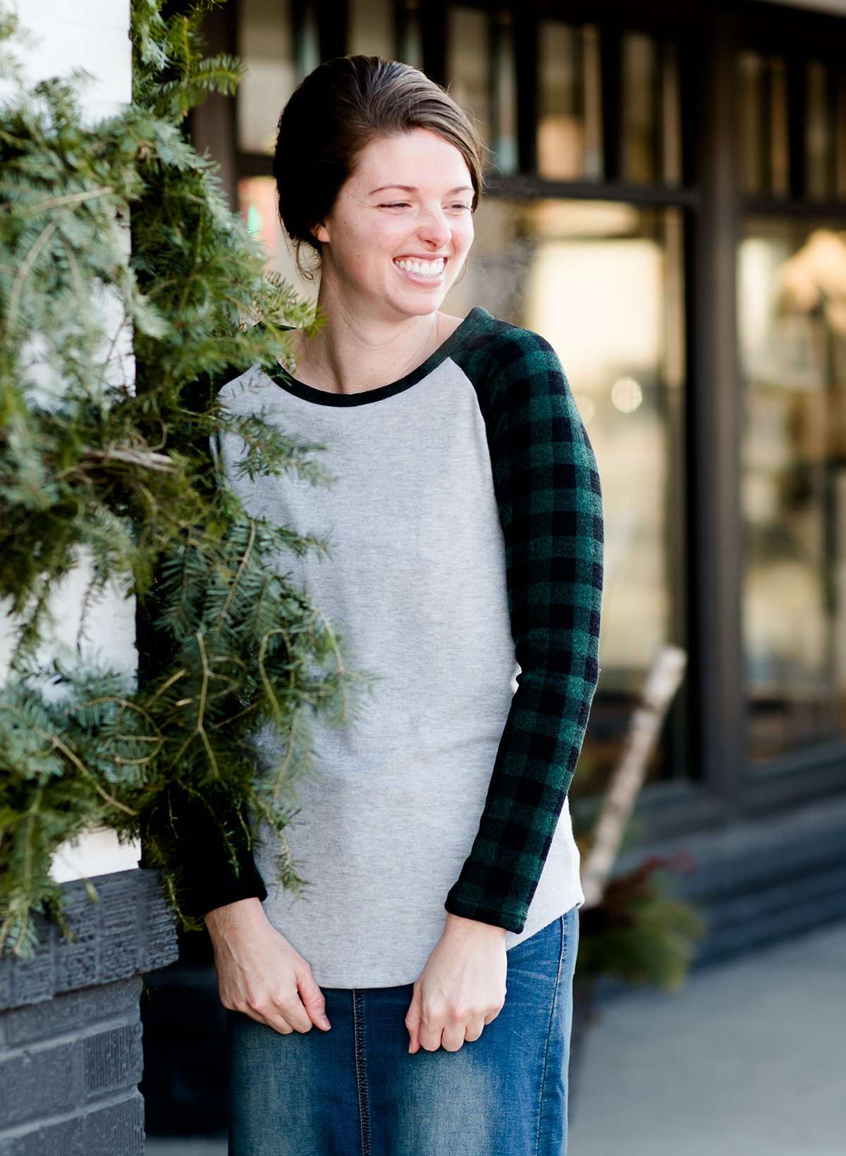 Woman wearing a black and green buffalo check sleeve raglan top paired with a long modest jean skirt standing outside of Inherit Clothing Company!