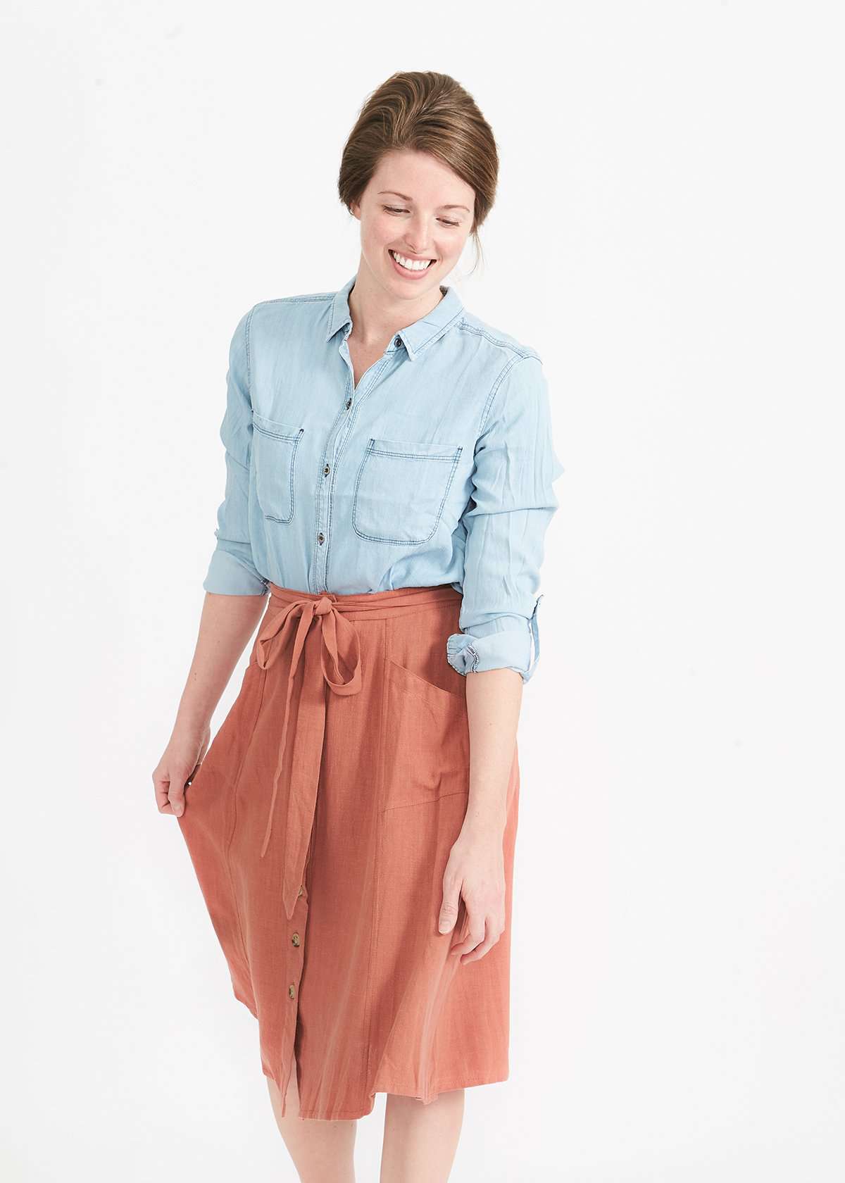Woman wearing a button front self tie pink midi skirt with big pockets and paired with dress heels and chambray top