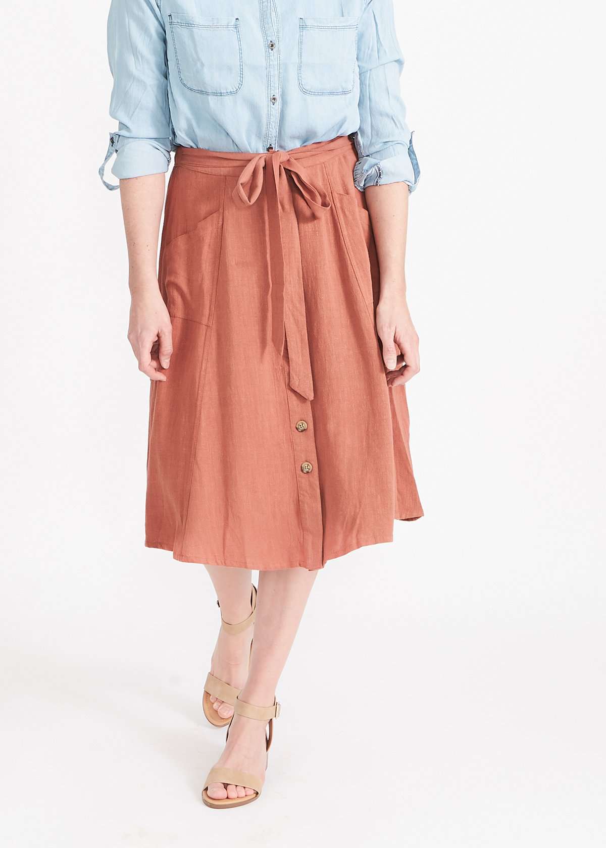 Woman wearing a button front self tie pink midi skirt with big pockets and paired with dress heels and chambray top