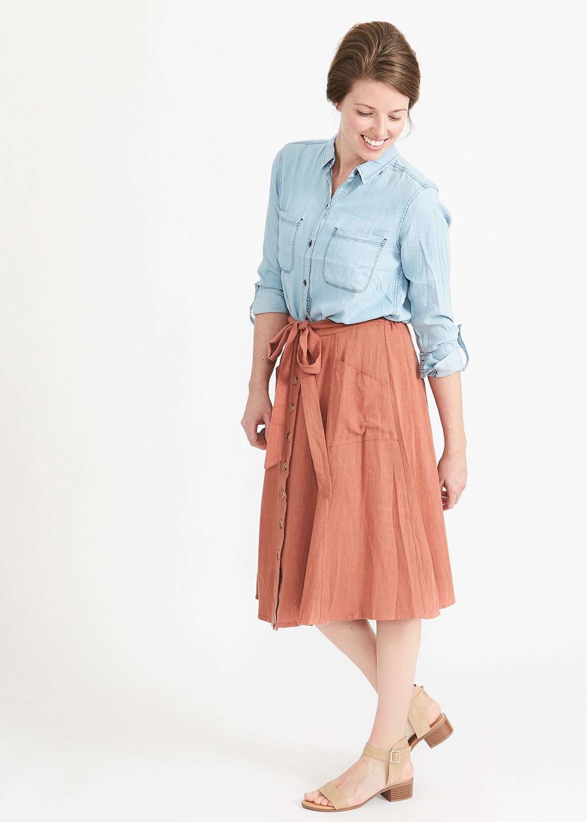 Woman wearing a button front self tie pink midi skirt with big pockets and paired with dress heels and chambray top