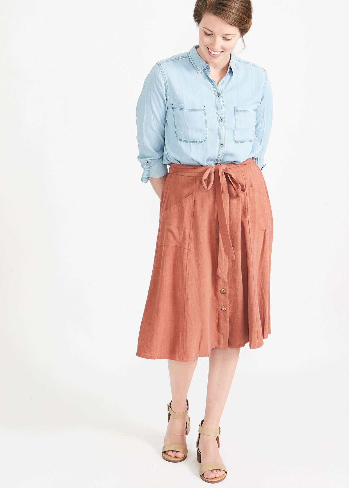 Woman wearing a button front self tie pink midi skirt with big pockets and paired with dress heels and chambray top
