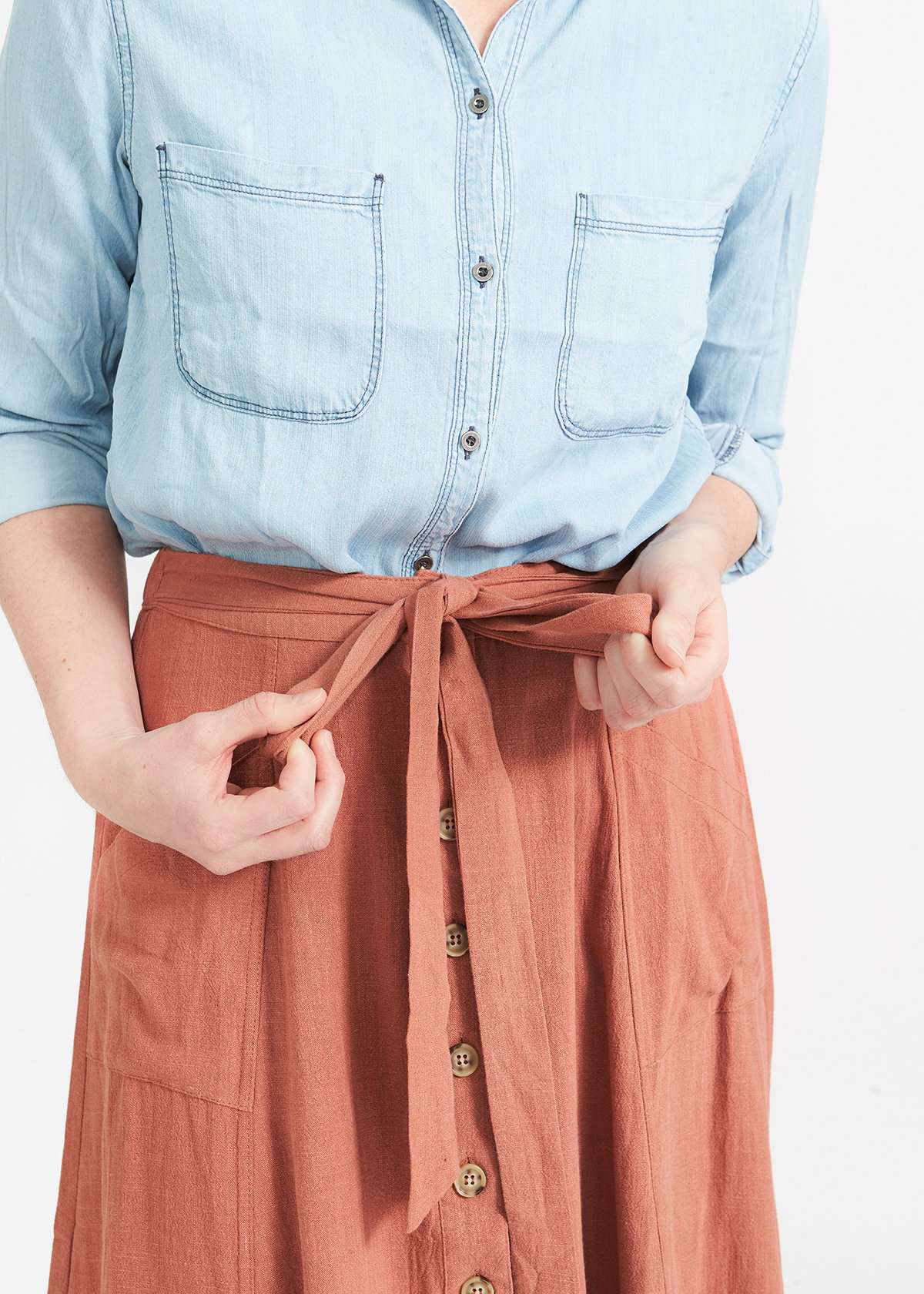 Woman wearing a button front self tie pink midi skirt with big pockets and paired with dress heels and chambray top