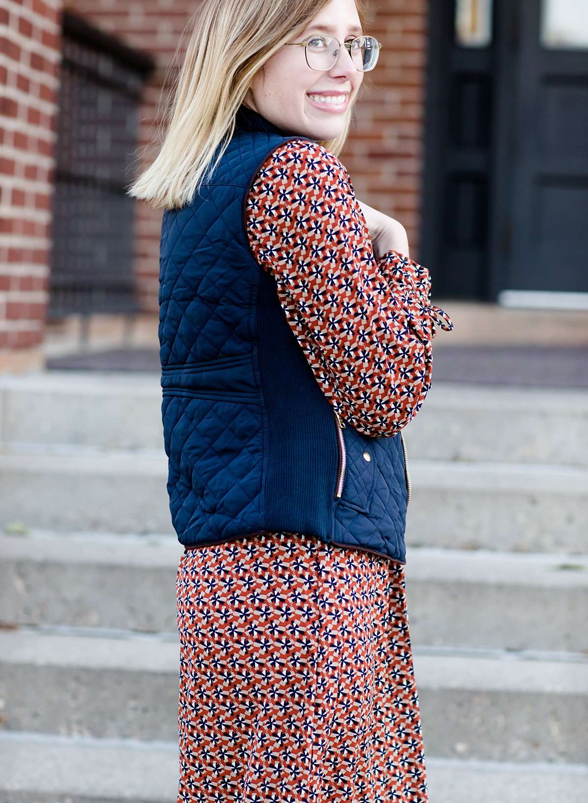 Woman wearing a cold weather, quilted puffer vest. This vest comes in mauve, black, navy and wine. It features pockets and a front zip.