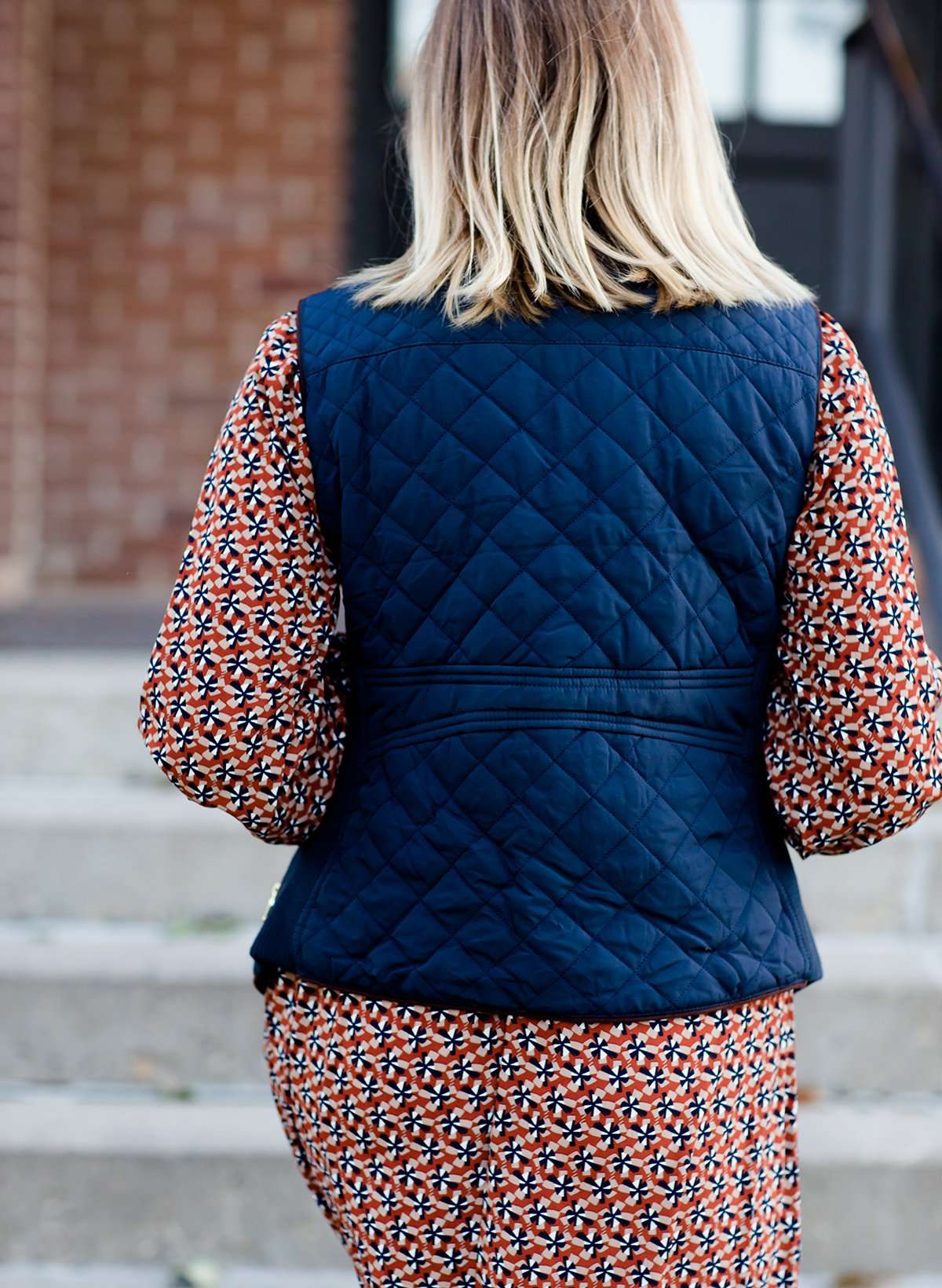 Woman wearing a cold weather, quilted puffer vest. This vest comes in mauve, black, navy and wine. It features pockets and a front zip.