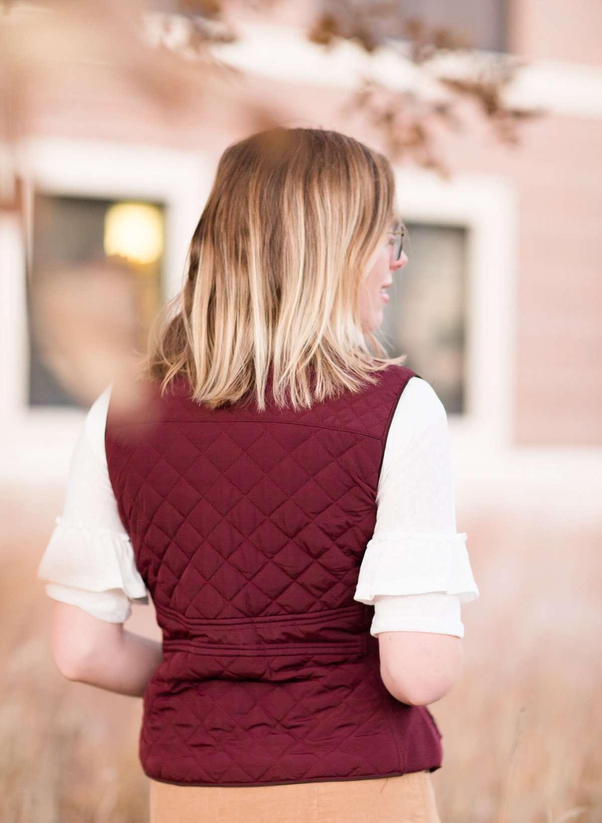 Woman wearing a cold weather, quilted puffer vest. This vest comes in mauve, black, navy and wine. It features pockets and a front zip.