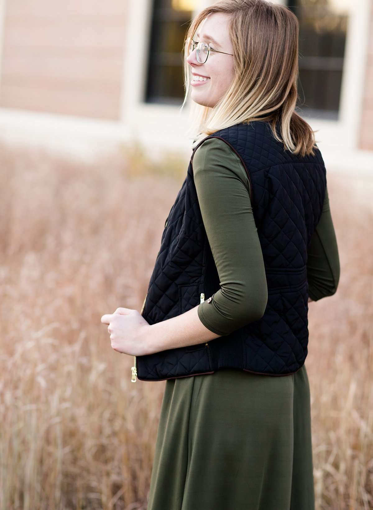Woman wearing a cold weather, quilted puffer vest. This vest comes in mauve, black, navy and wine. It features pockets and a front zip.