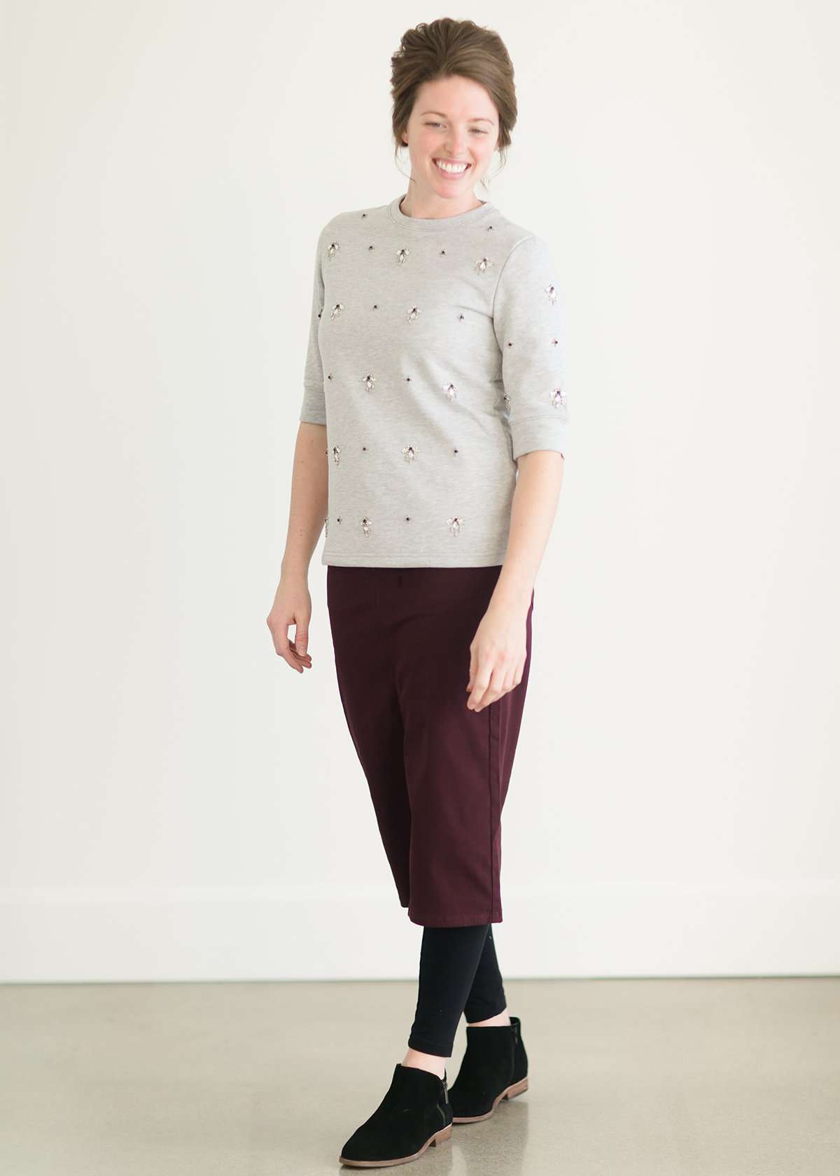 Woman wearing a gray crew neck sweatshirt that is half sleeves and has jewel designs on it.