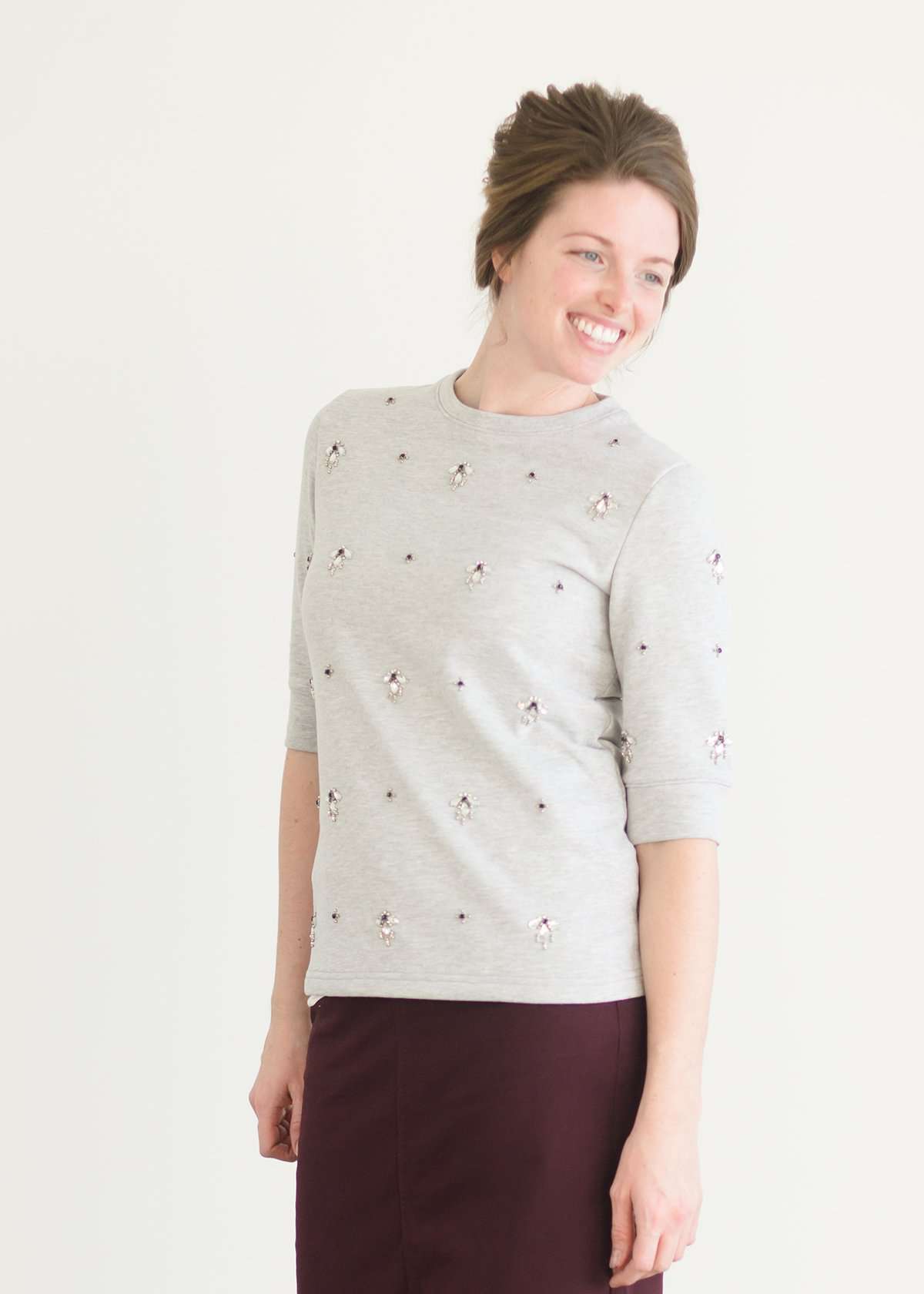Woman wearing a gray crew neck sweatshirt that is half sleeves and has jewel designs on it.