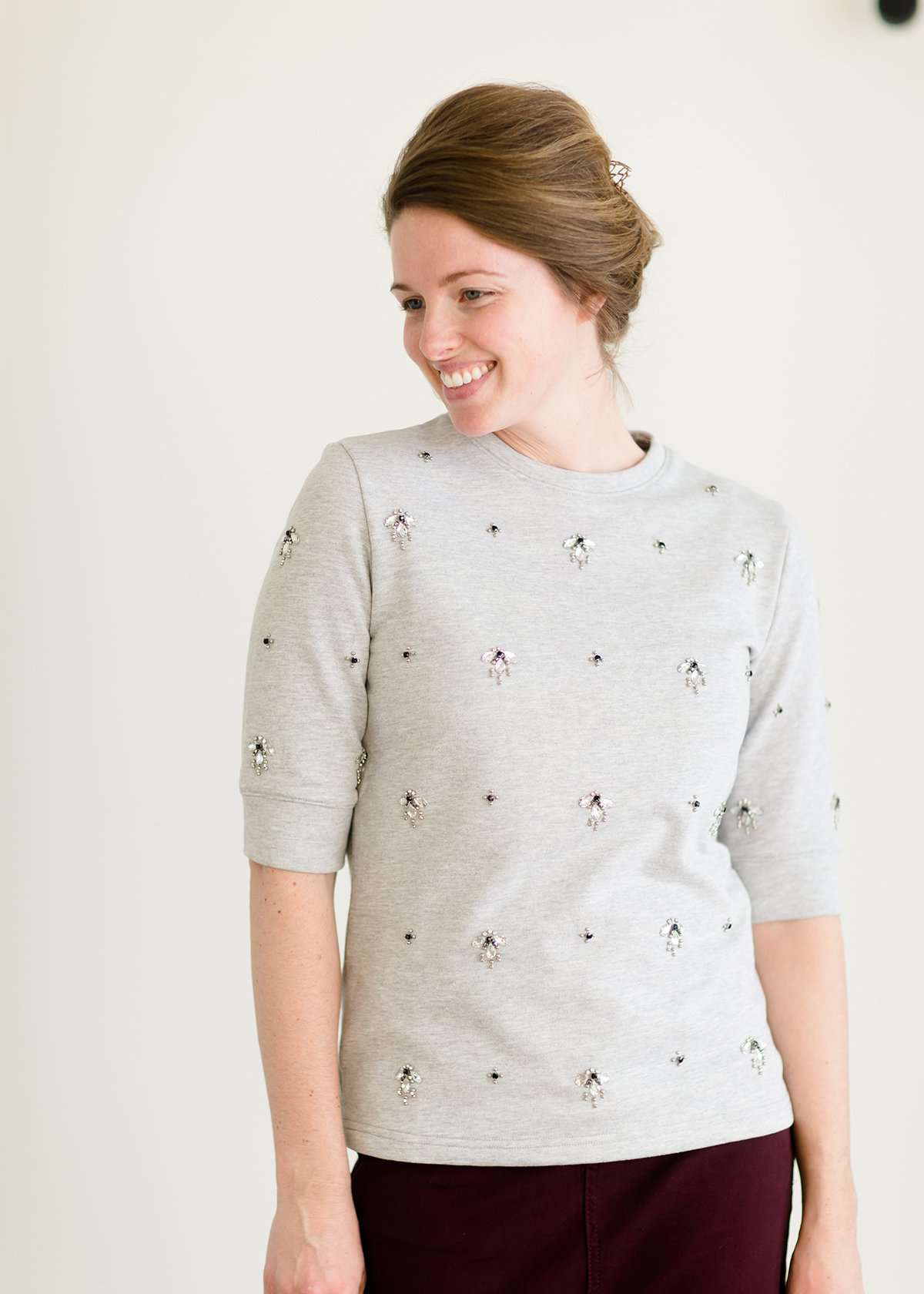 Woman wearing a gray crew neck sweatshirt that is half sleeves and has jewel designs on it.