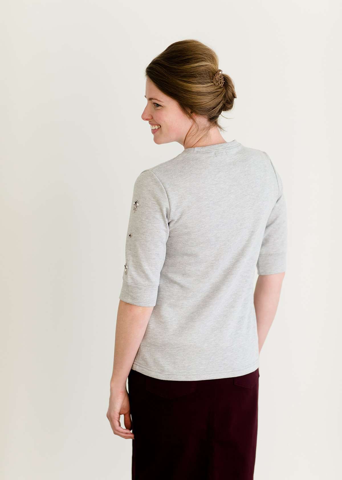 Woman wearing a gray crew neck sweatshirt that is half sleeves and has jewel designs on it.