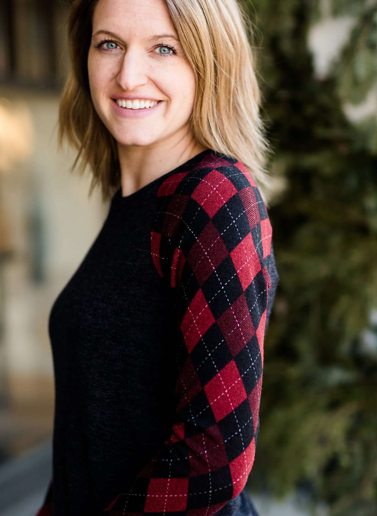 Woman wearing a dark charcoal raglan style top with diamond, argyle checks that are black and red. She is standing outside of Inherit Clothing Company.