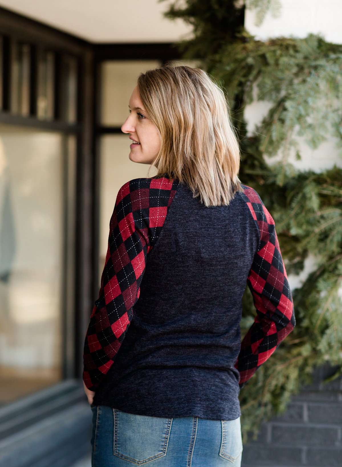Woman wearing a dark charcoal raglan style top with diamond, argyle checks that are black and red. She is standing outside of Inherit Clothing Company.