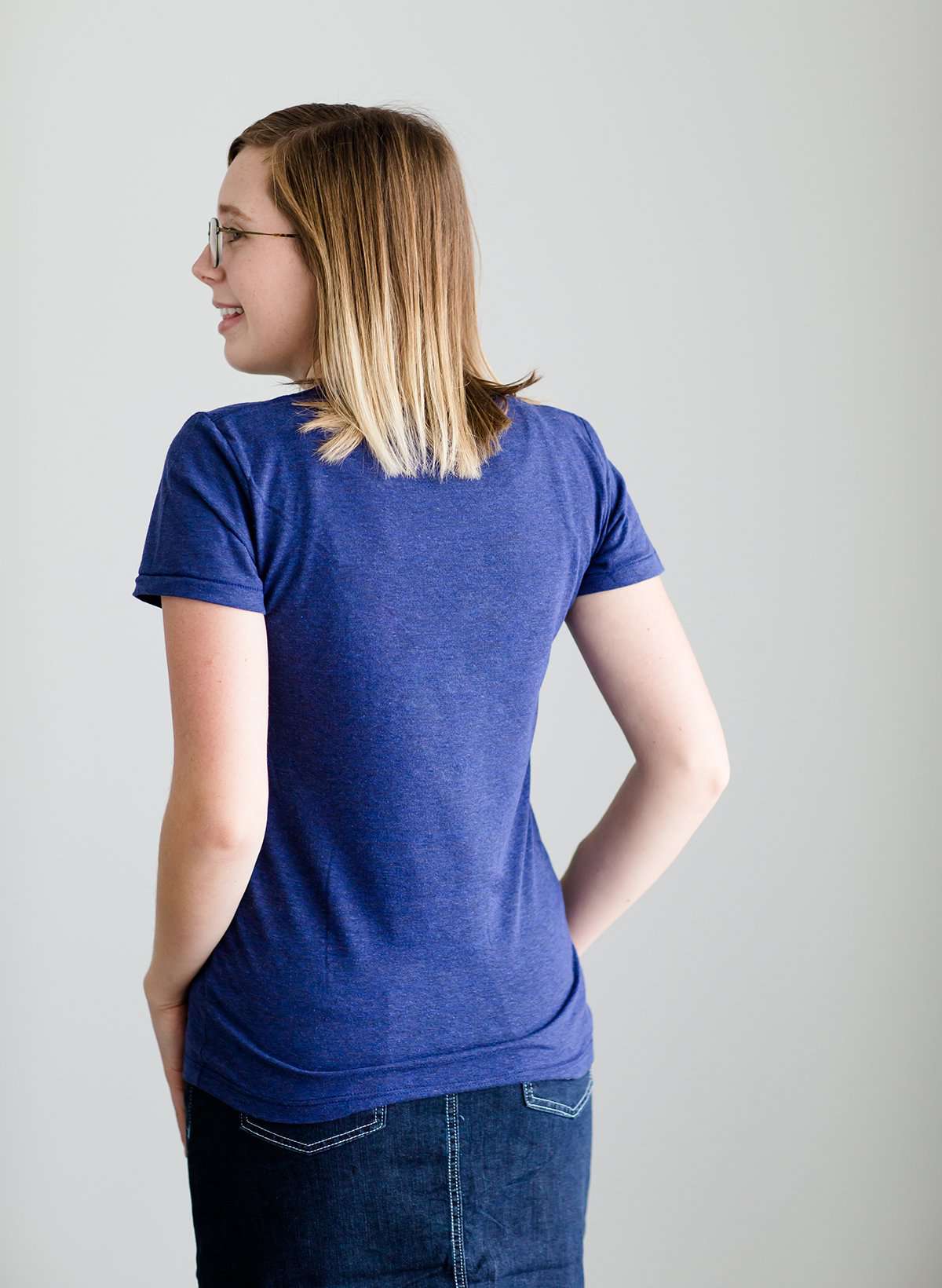 Young woman wearing a blue graphic tee with yellow words that says "Do Good." It is also paired with a below the knee denim skirt and a plaid button up top.