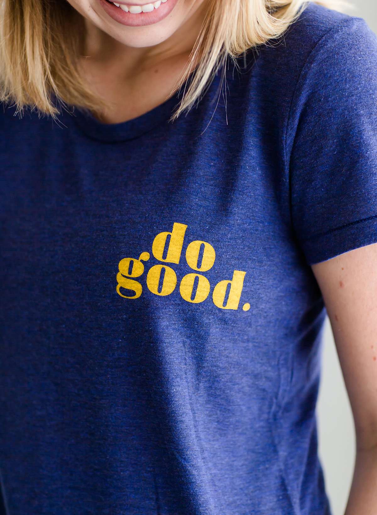Young woman wearing a blue graphic tee with yellow words that says "Do Good." It is also paired with a below the knee denim skirt and a plaid button up top.