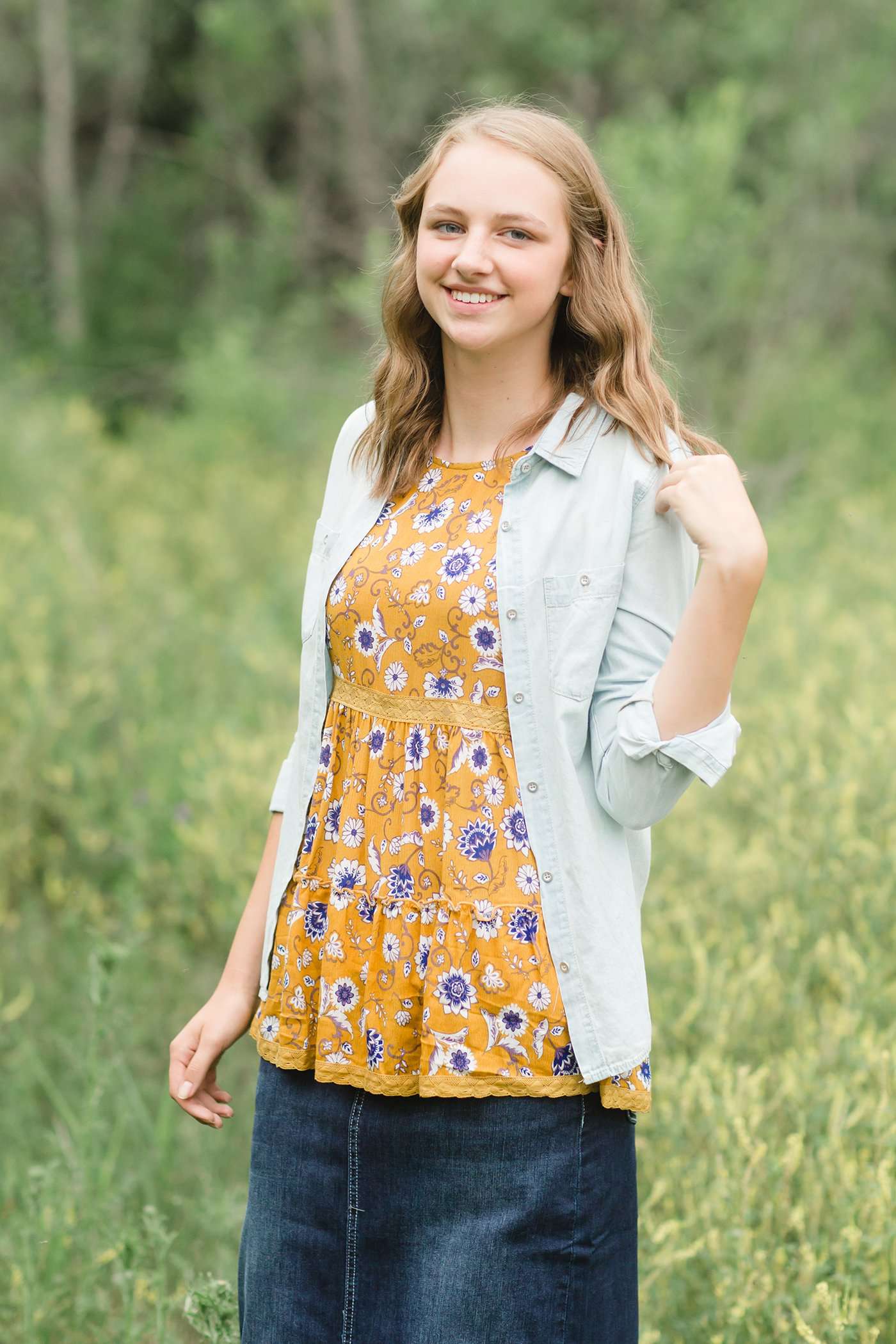 young woman wearing a mustard color tank with blue and white florals. There is embroidered detail just below the chest.