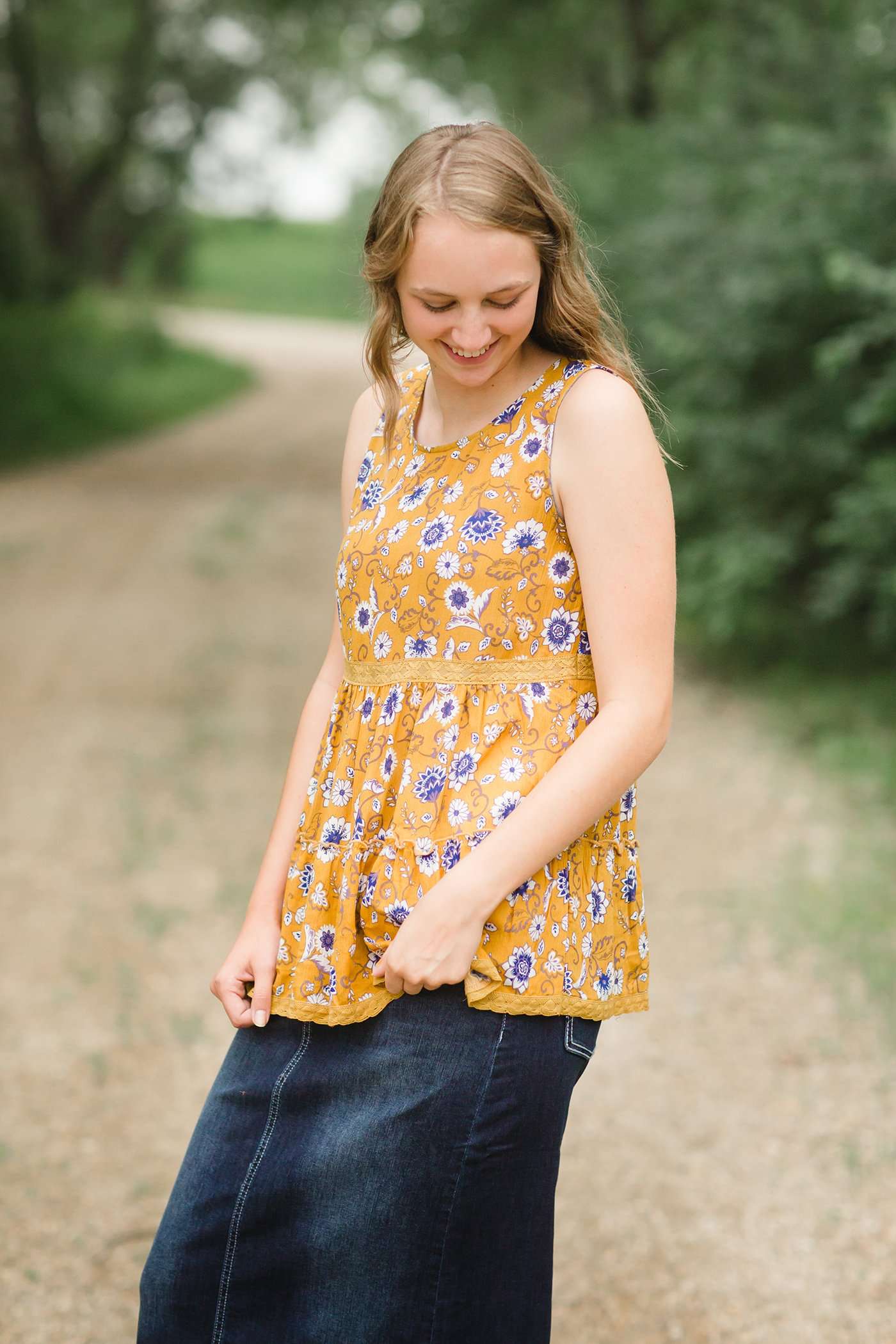 young woman wearing a mustard color tank with blue and white florals. There is embroidered detail just below the chest.