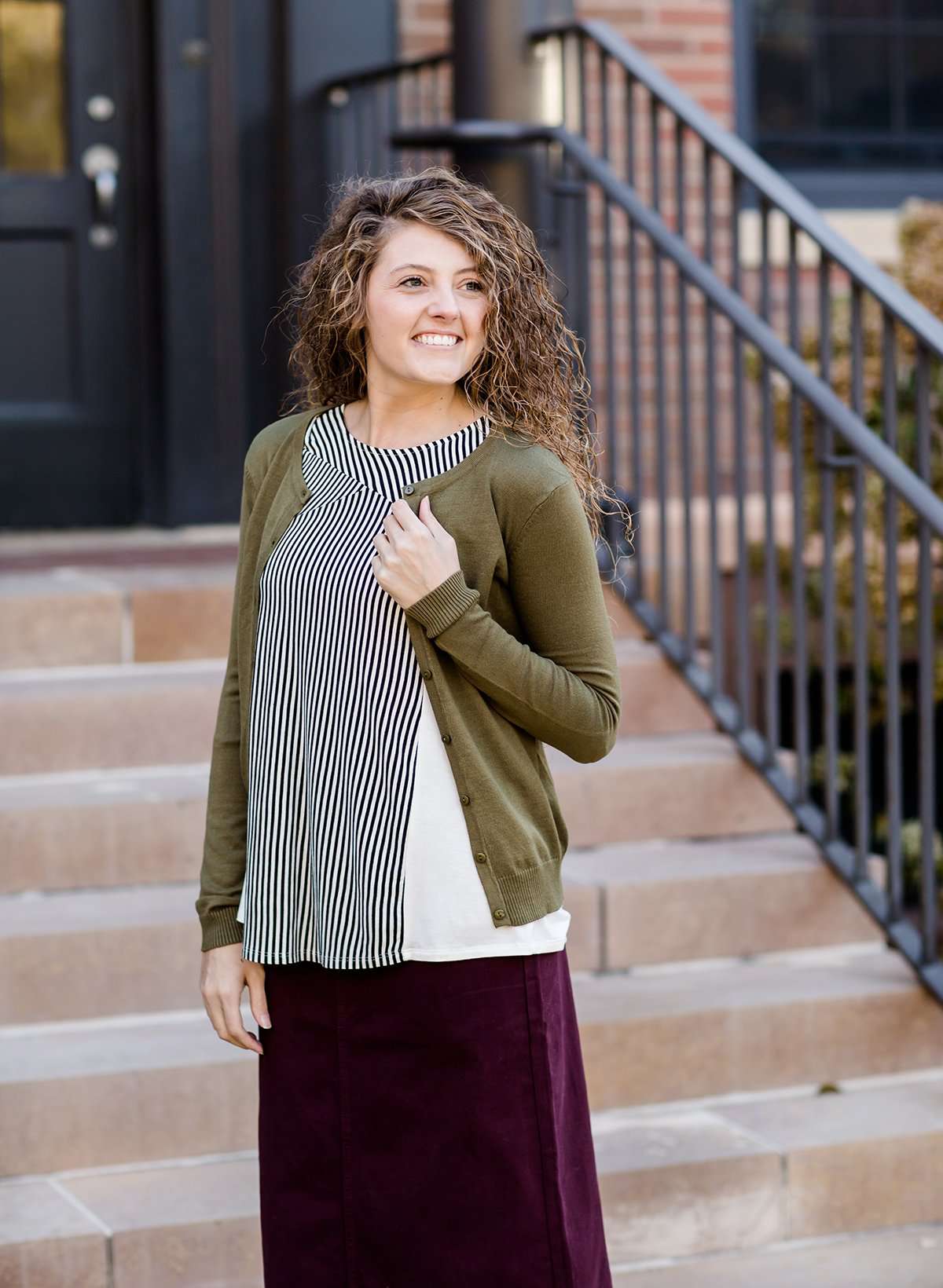 Woman wearing a modest and classic pink, burgandy, emerald and olive colored button up crewneck cardigan with a midi skirt