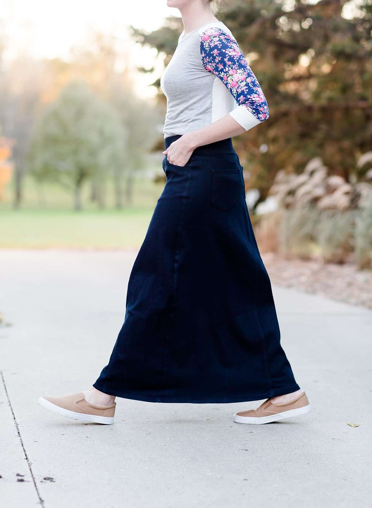 Women wearing a long dark blue denim skirt that is a-line and has flare. This modest skirt is also paired with a floral and gray raglan tee.