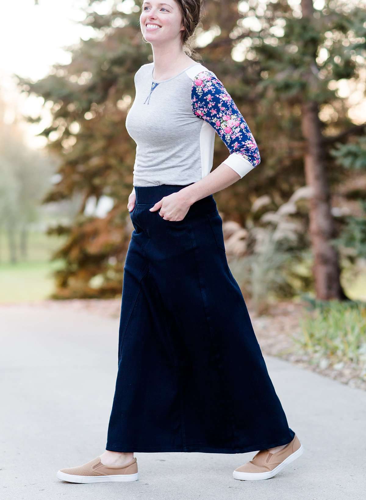 Women wearing a long dark blue denim skirt that is a-line and has flare. This modest skirt is also paired with a floral and gray raglan tee.