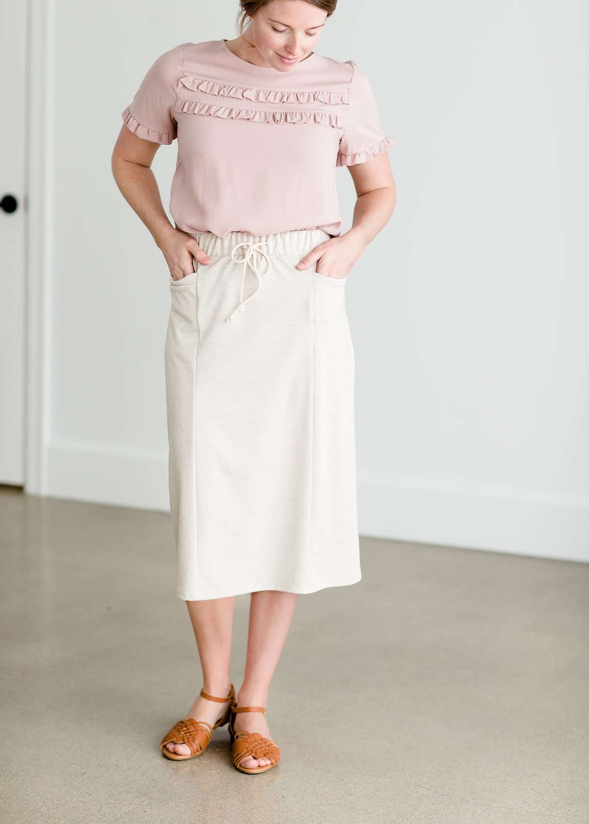 Woman wearing a cream colored french terry below the knee skirt with front ties, front panels and pockets!
