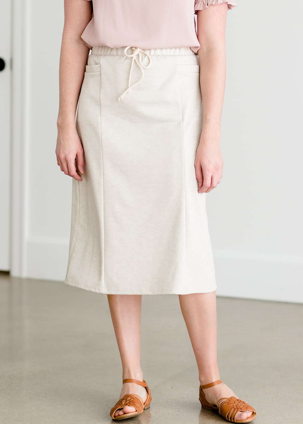 Woman wearing a cream colored french terry below the knee skirt with front ties, front panels and pockets!