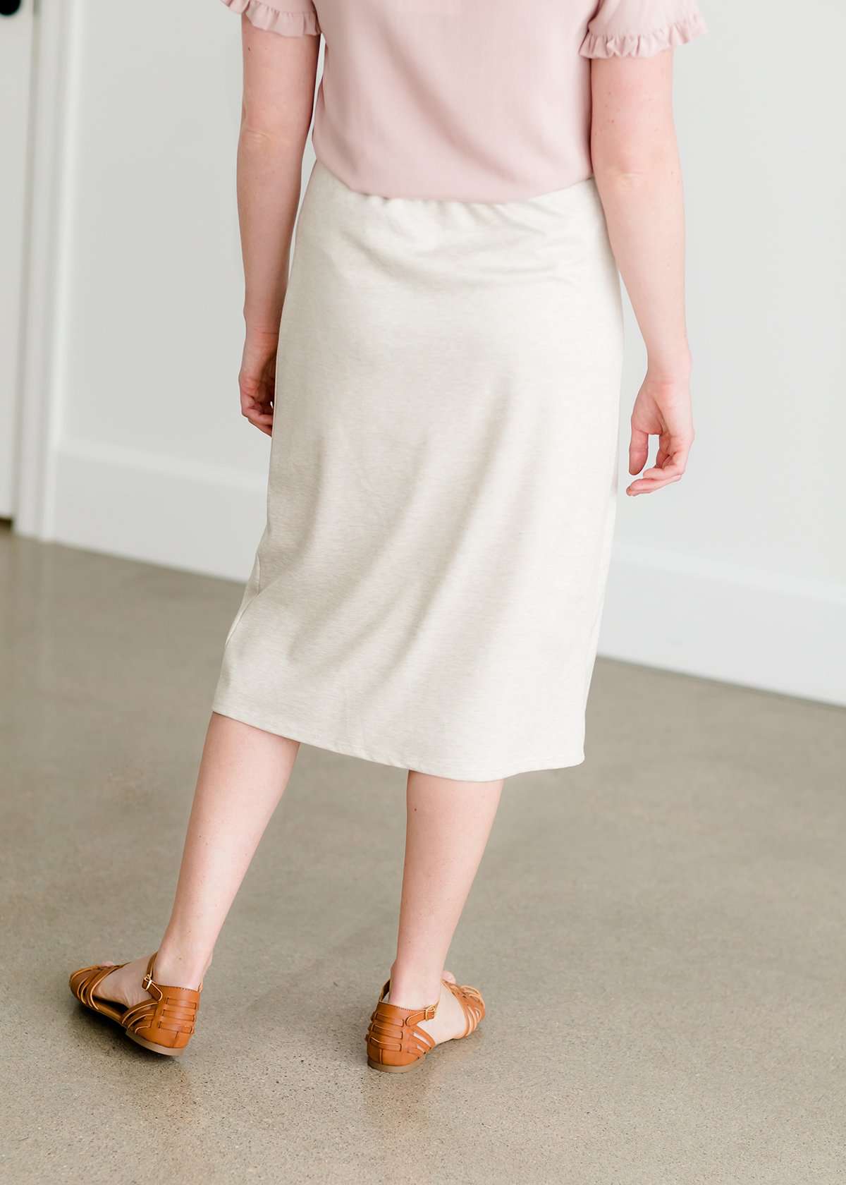 Woman wearing a cream colored french terry below the knee skirt with front ties, front panels and pockets!