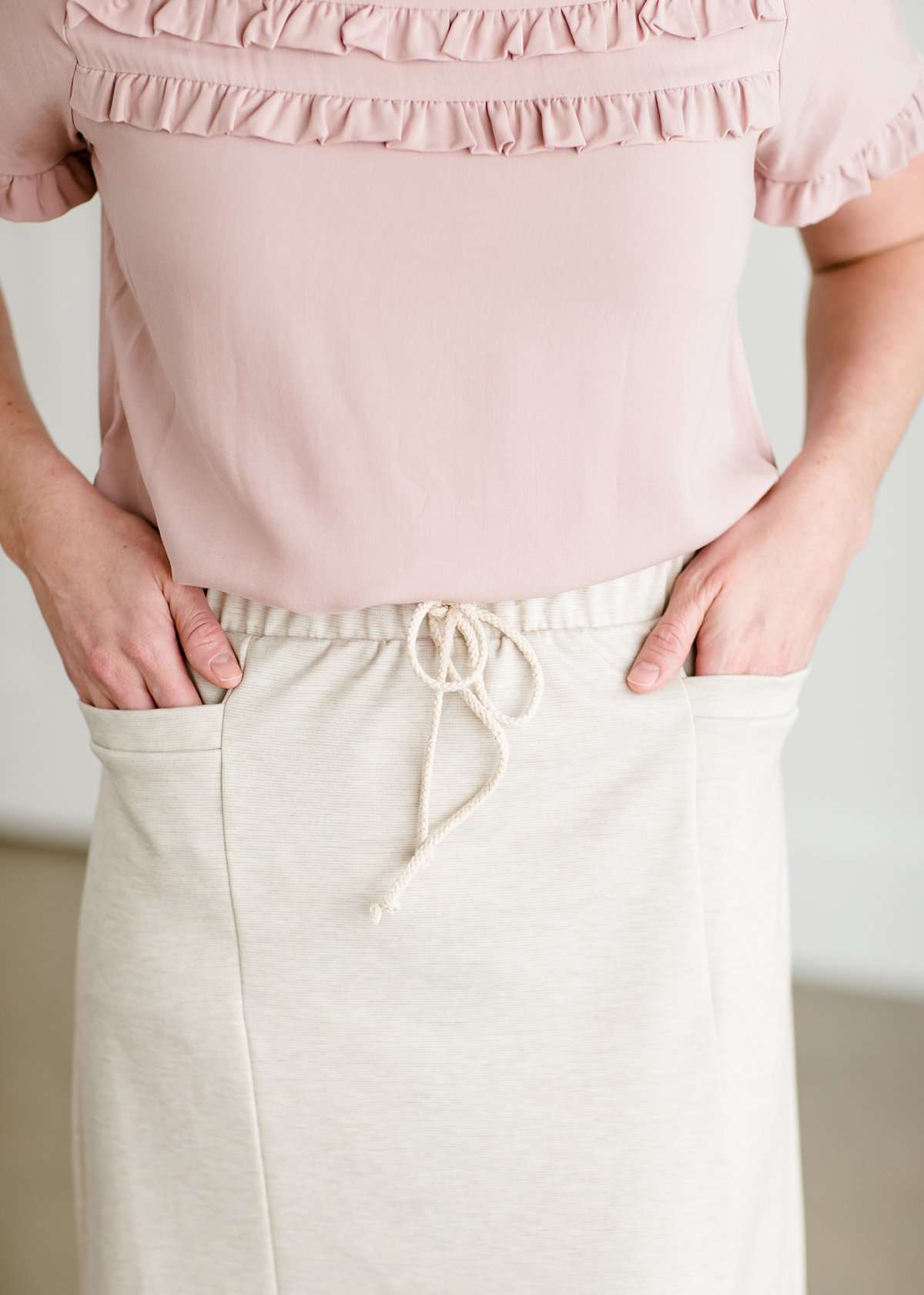 Woman wearing a cream colored french terry below the knee skirt with front ties, front panels and pockets!