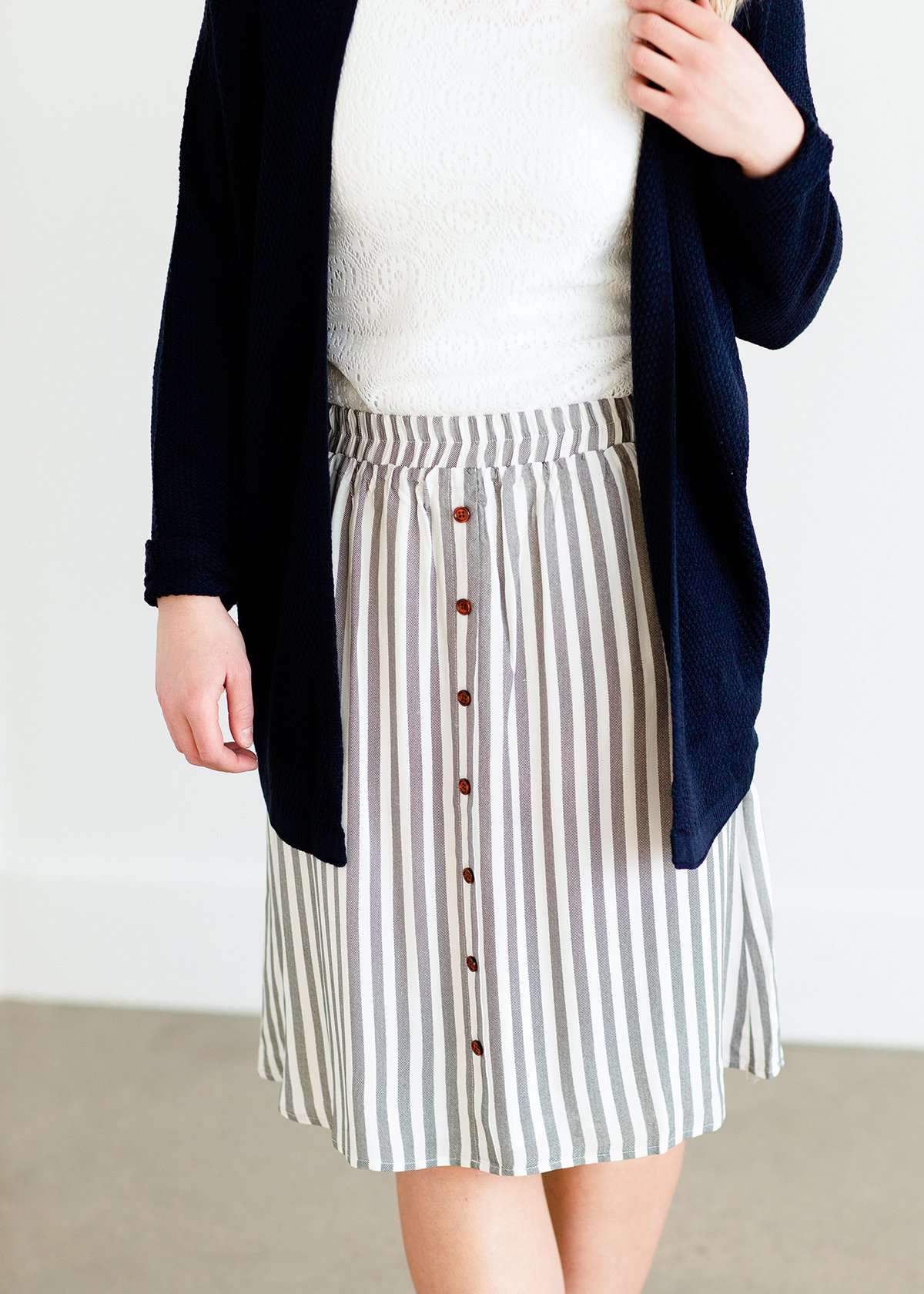 Woman wearing a gray striped skirt with camel colored faux buttons on the front that also has an elastic waistband
