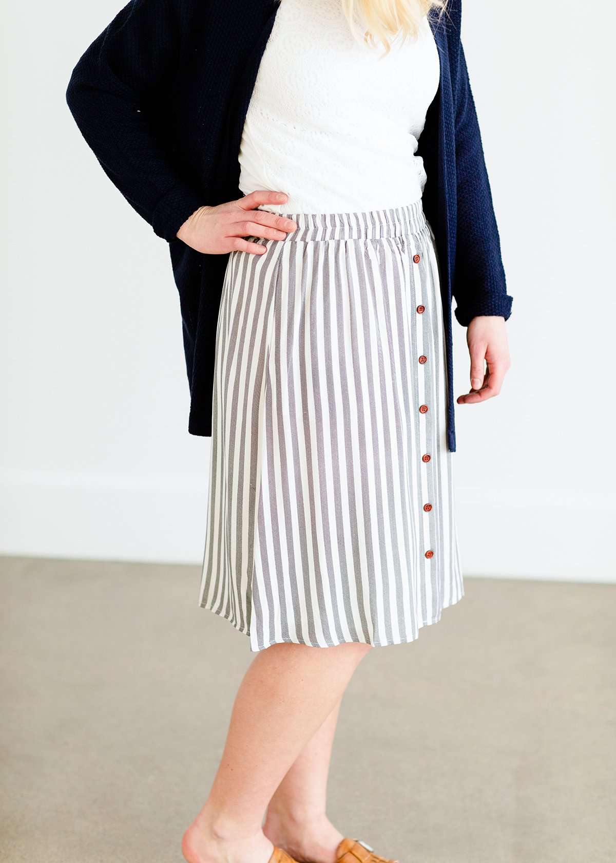 Woman wearing a gray striped skirt with camel colored faux buttons on the front that also has an elastic waistband