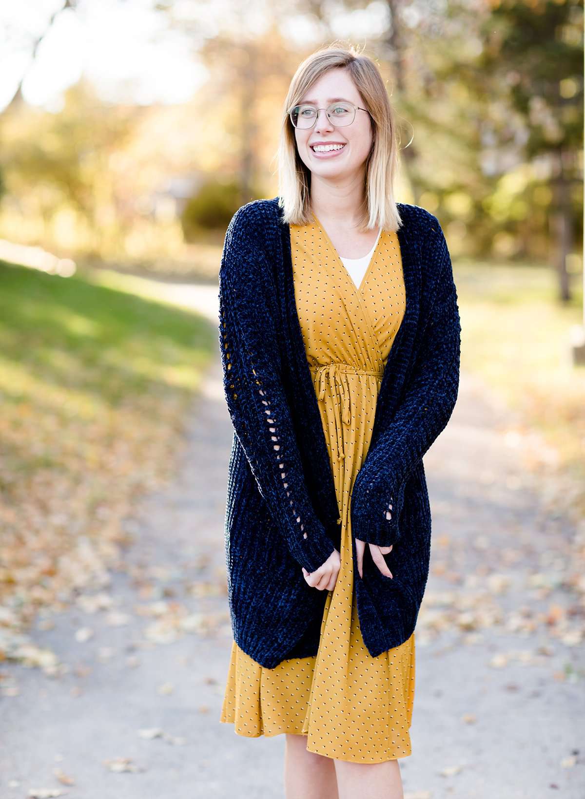 Young woman wearing a modest golden printed midi dress that has a faux wrap and is nursing friendly