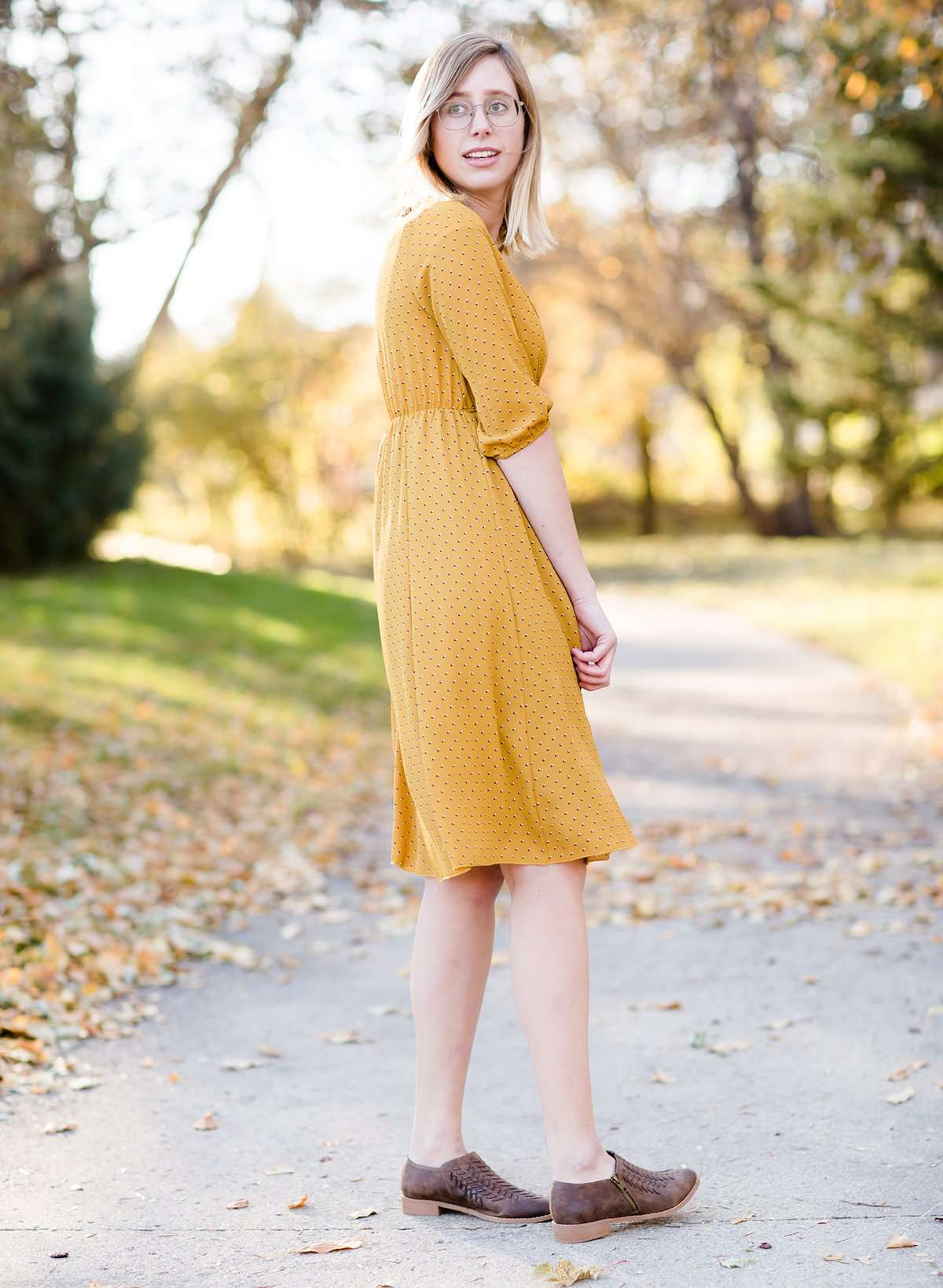 Young woman wearing a modest golden printed midi dress that has a faux wrap and is nursing friendly
