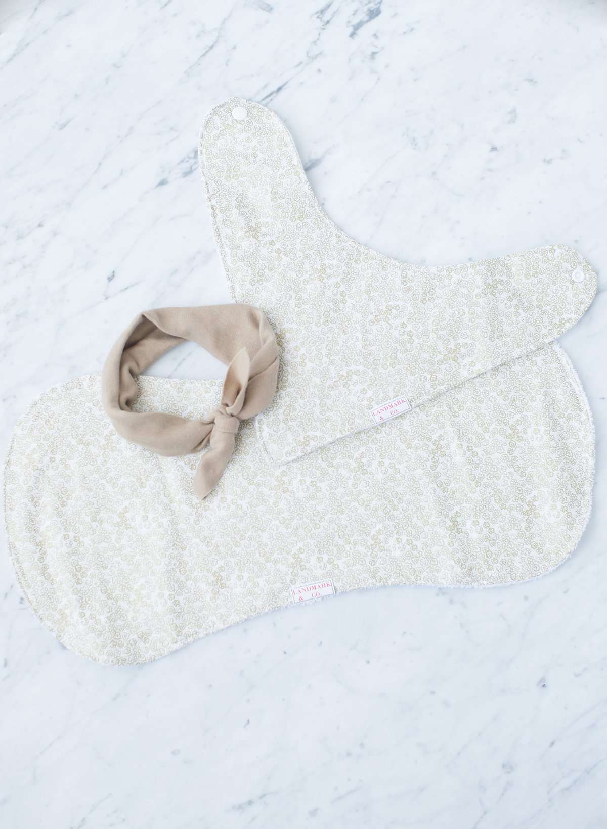 This baby gift set features a burp cloth, bib bandana and a headband. It is oatmeal colored fabric with gold foil like florals all over.