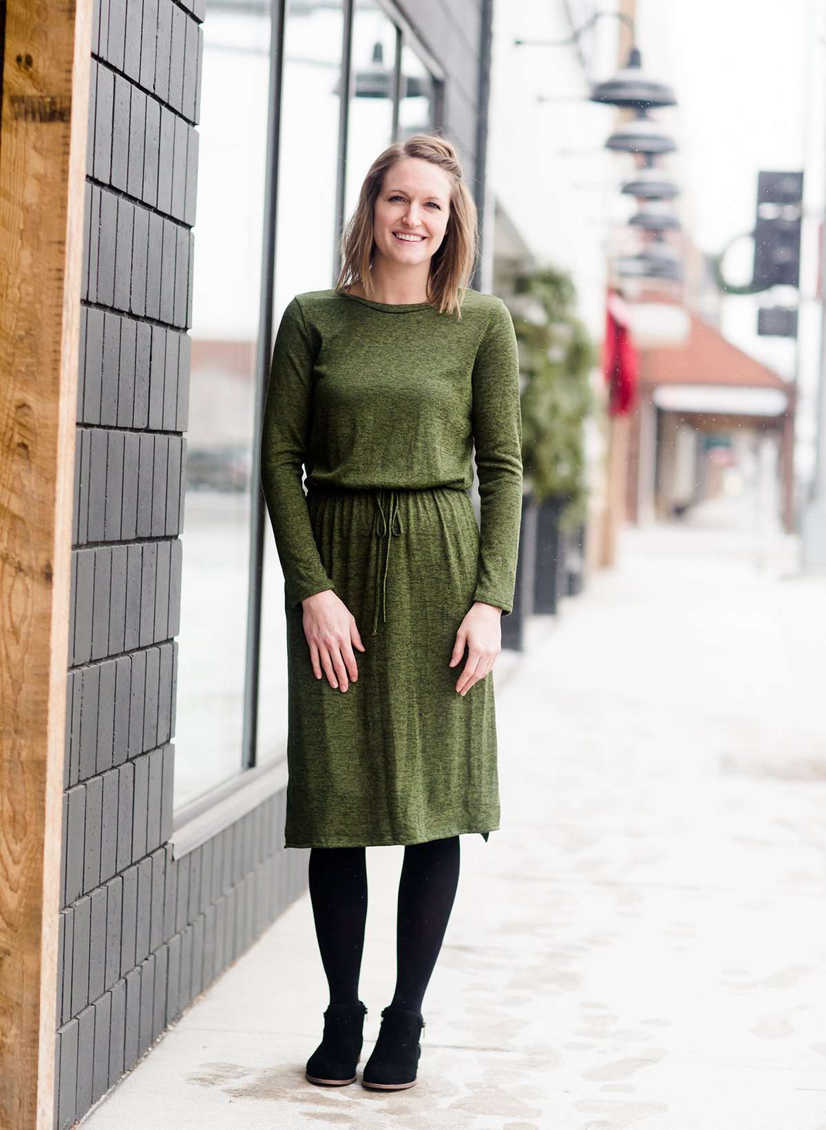 Woman wearing a olive colored hacci midi dress with a elastic waist and paired with black sole society boots