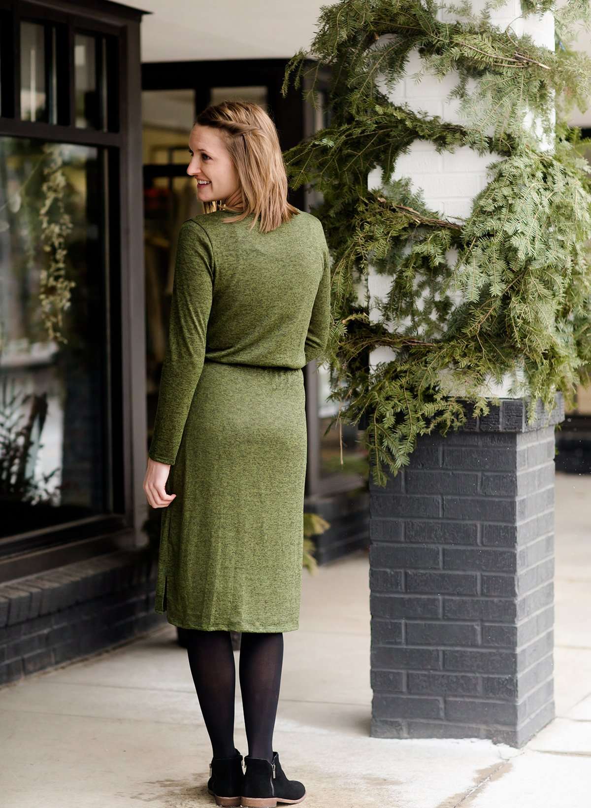 Woman wearing a olive colored hacci midi dress with a elastic waist and paired with black sole society boots