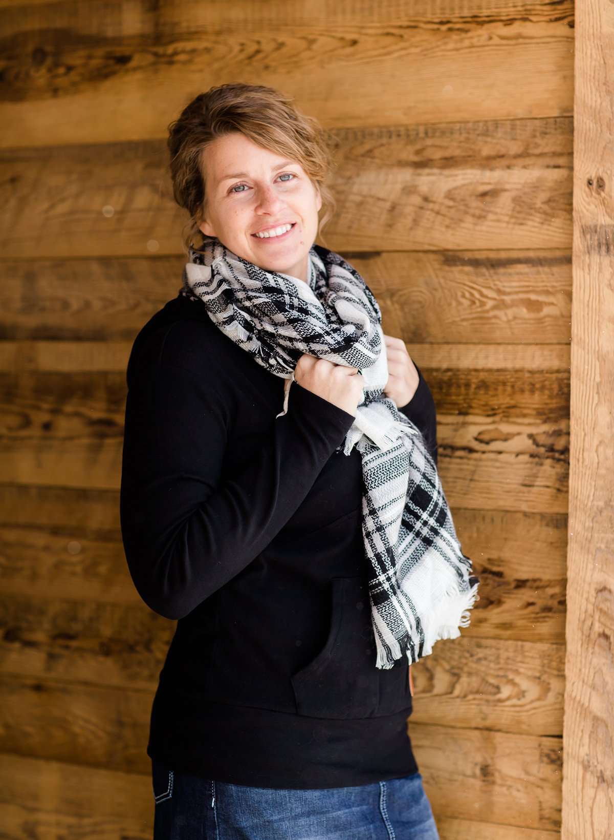Woman wearing a black, Ampersand half zip, back sweatshirt. It has white toggle strings and a front kangaroo pouch pocket. It is also paired with a long modest jean skirt.