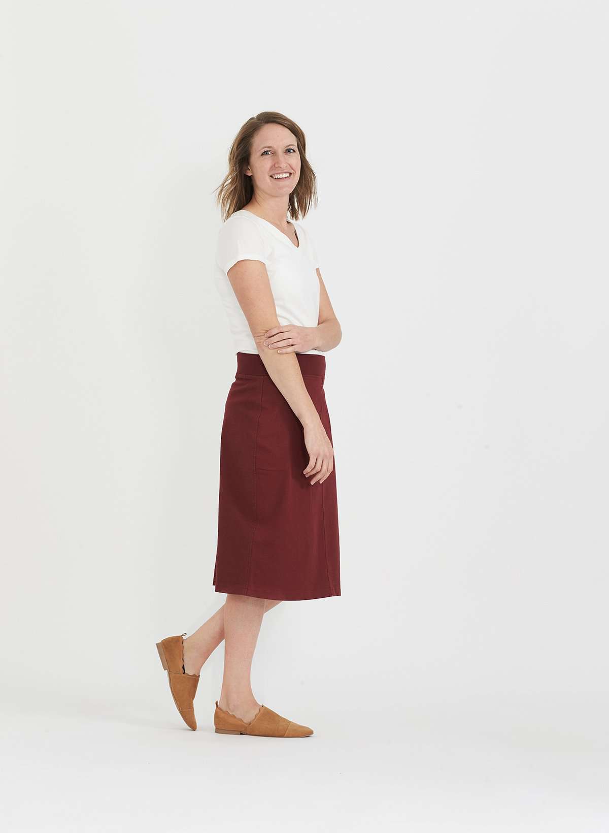 Woman wearing a colored, denim-like skirt with a elastic waistband. This is a modest skirt that falls below the knee. It comes in Burgundy, olive, khaki, black and navy. It is also paired with a white v-neck t-shirt.